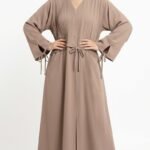 Taupe nida abaya with V-neckline, pin-tuck pleats on one side of the bodice, front bow tie and tie-detail cuffs